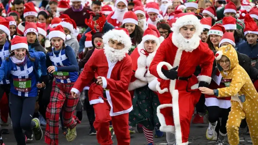 Une course festive de Noël à Lausanne avec des participants joyeux déguisés en Père Noël, rennes, et d'autres personnages festifs, débutant la course avec énergie et esprit de fête.